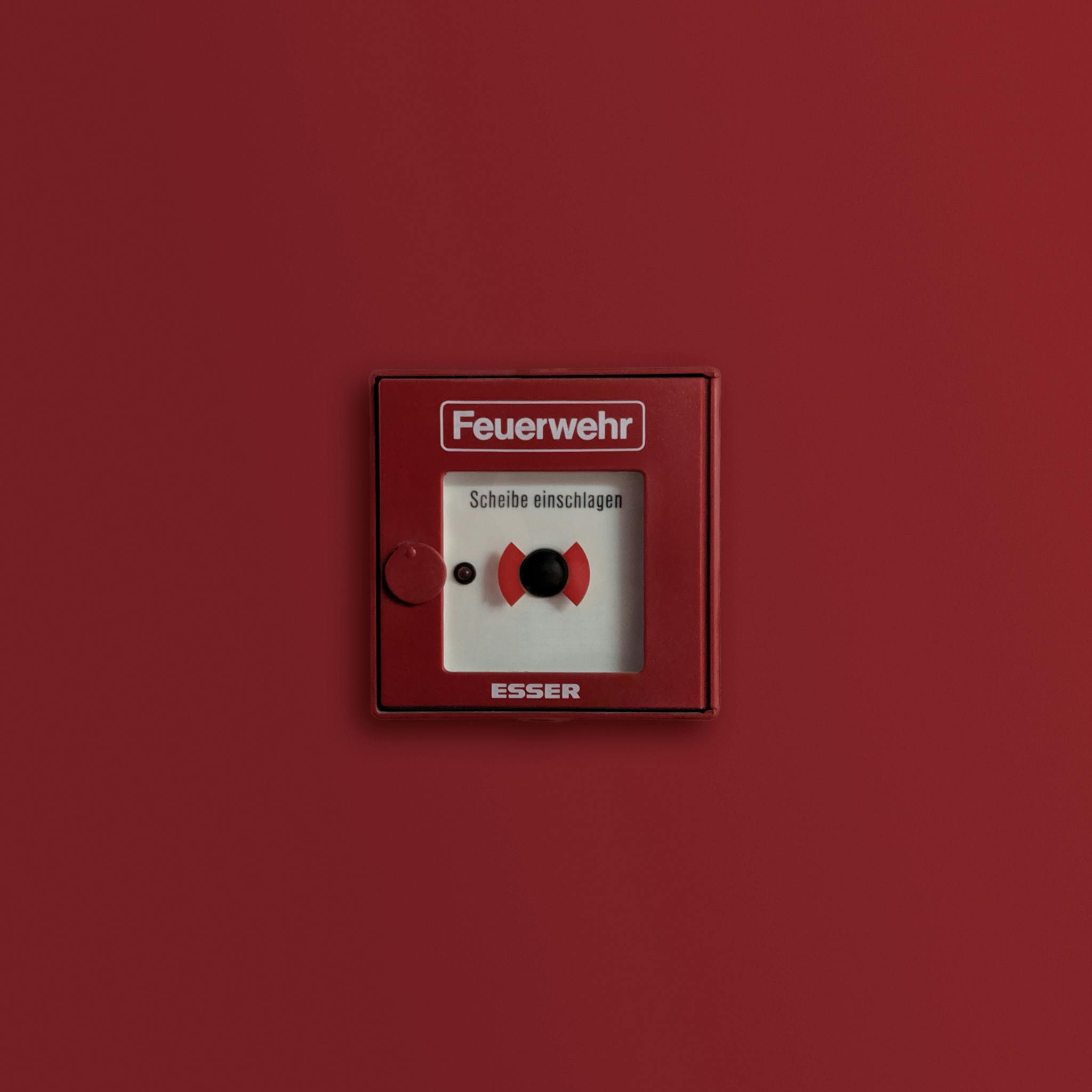 Red fire alarm panel indicating emergency system on solid background.