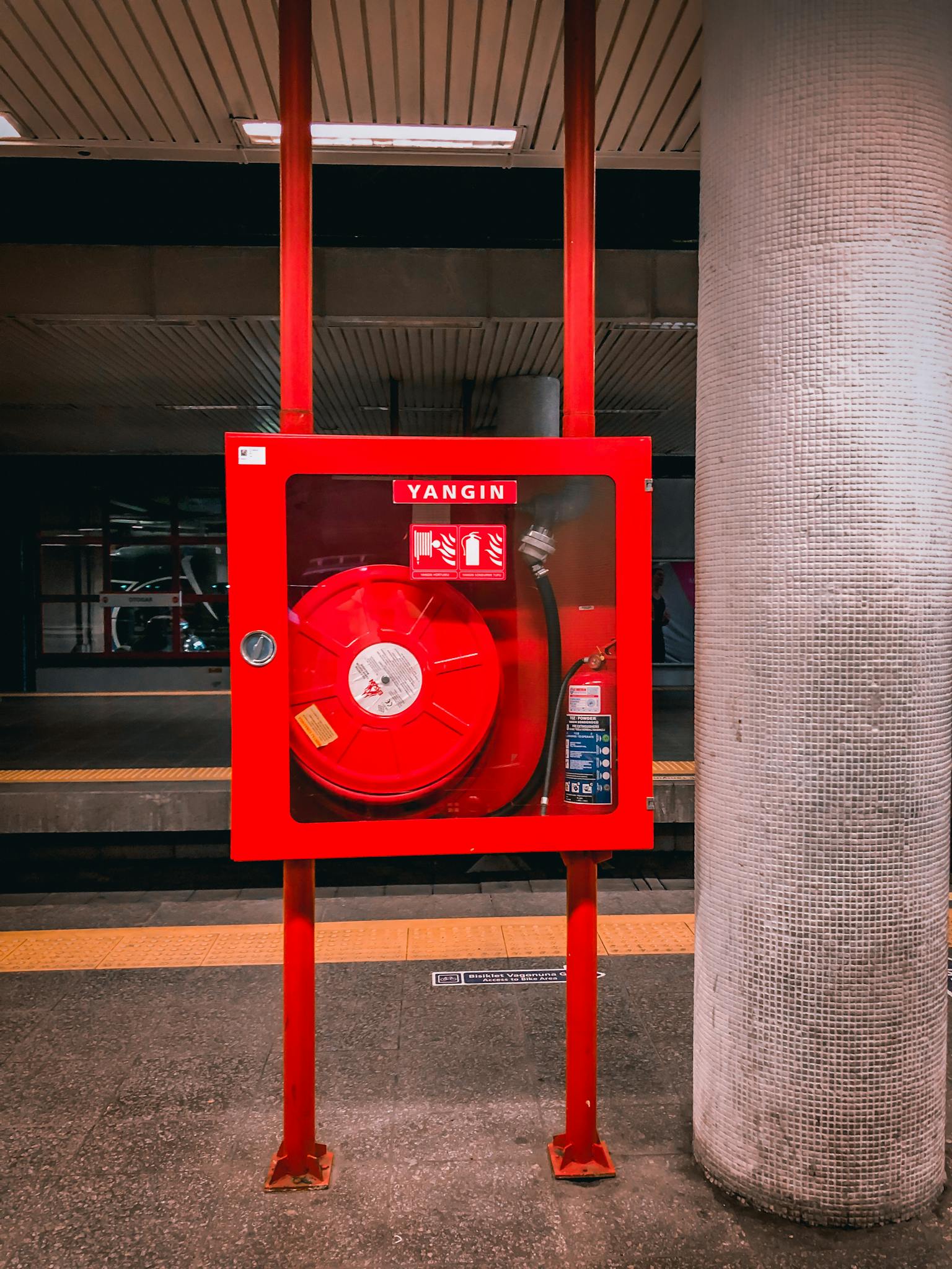 Vibrant red fire hose reel stationed in an empty subway platform for safety preparedness.